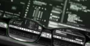 Eine Brille liegt auf der Laptooptastatur und durch die Gläser wird die Desktopzeile scharf. Alles andere ist verschwommen.