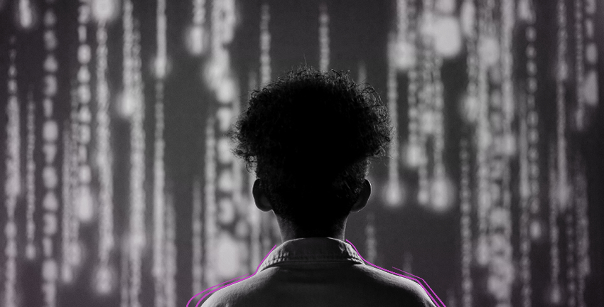 Eine Frau mit Afro steht im Kittel vor einem grßen Bildschirm. Auf ihm befinden sich senkrechte Zahlen, die verschwommen dargestellt sind.